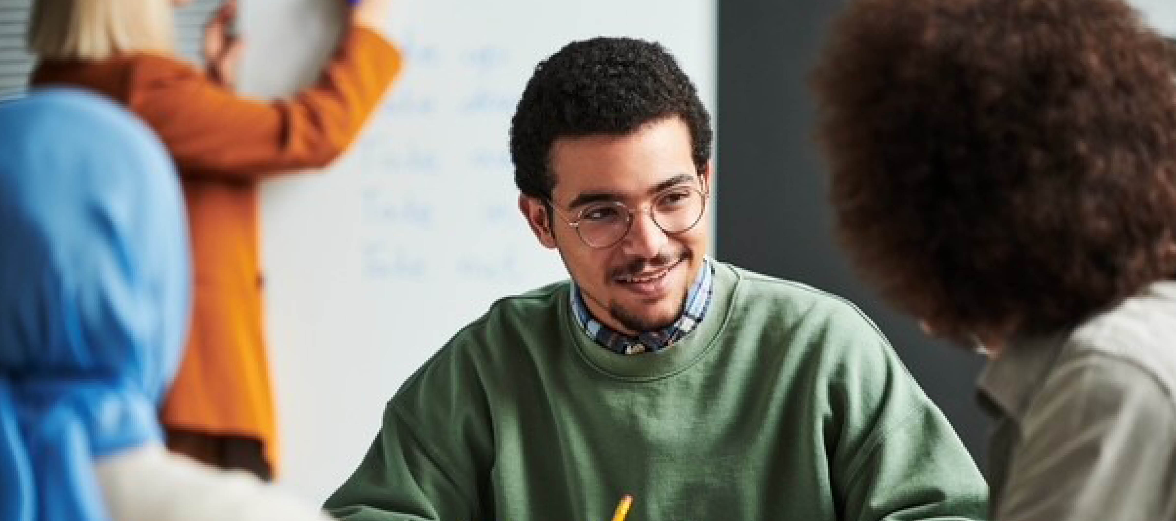 Dunkelhaariger Mann mit Brille sitzt mit zwei weiteren Personen an einem Tisch